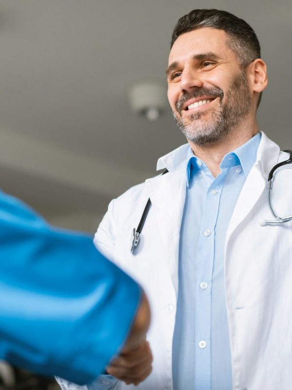 Happy male chief medical officer hiring welcoming new teammate in clinic