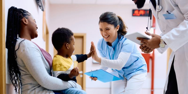 Happy nurse giving high-five to small black boy at medical clinic.