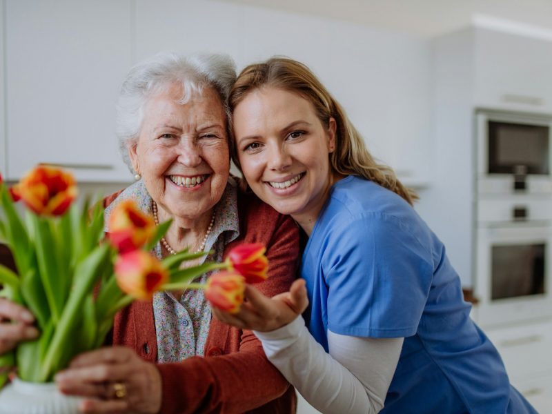 Senior woman and nurse with tulip bouquet.